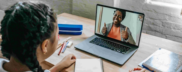 Young woman sitting in front of a computer on a video call with another woman who is smiling and giving two thumbs up