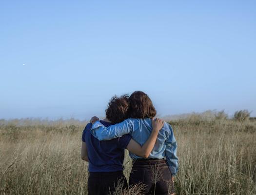 Relationships two people stood with their arms around each other looking into the distance while stood in a field